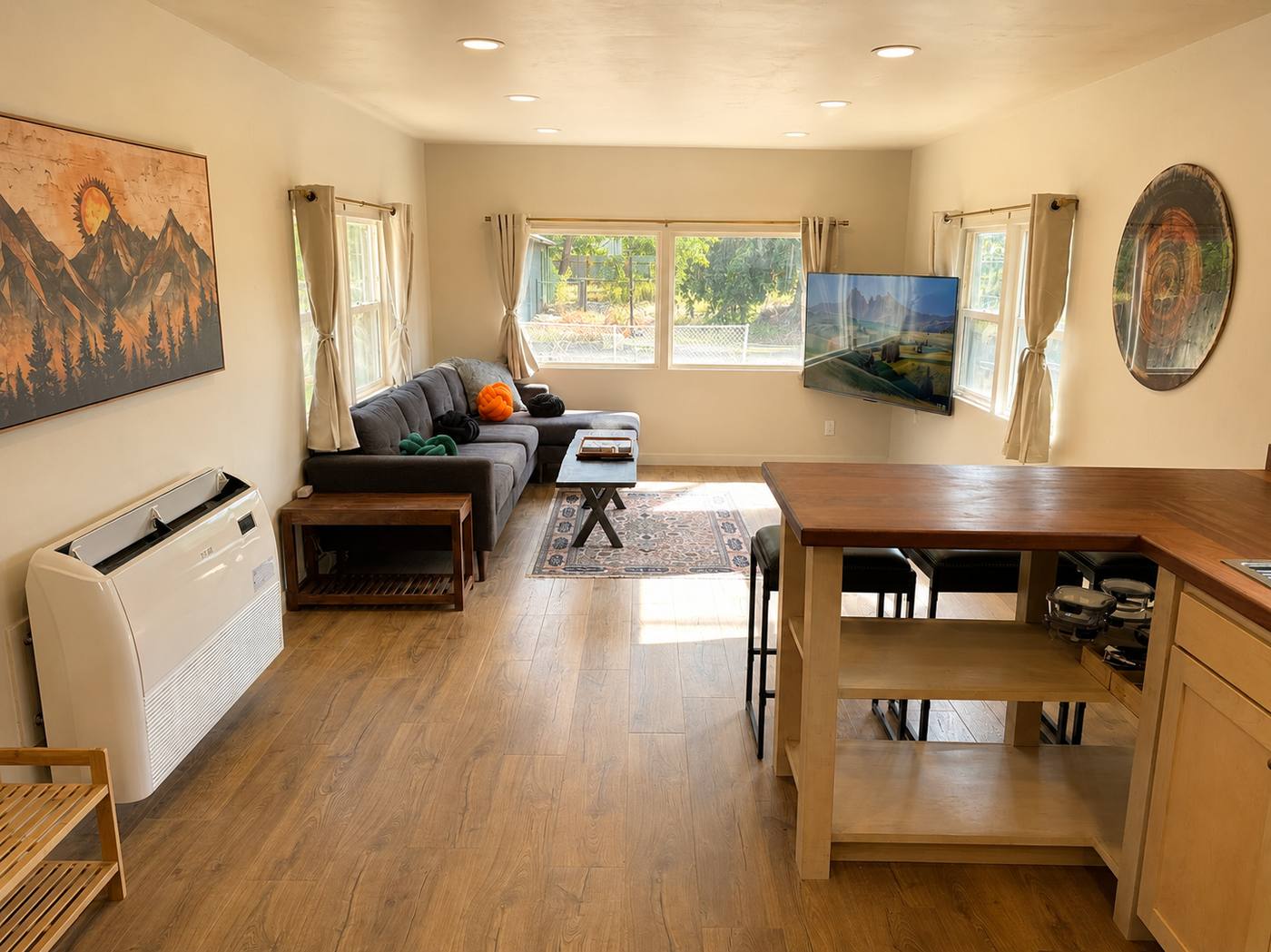 Open living room and kitchen with wood-look floors, mini-split unit and wall-mounted TV