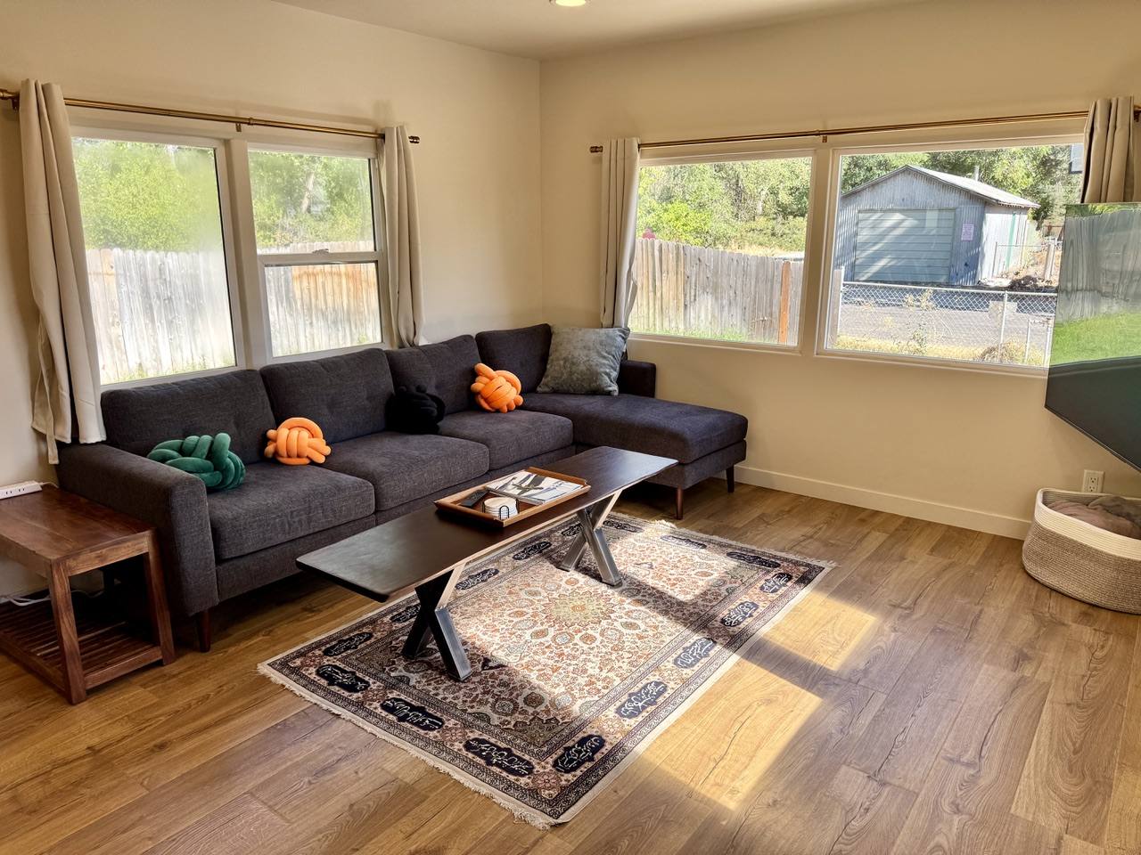 Grey sectional sofa and coffee table on a patterned rug, windows on two walls