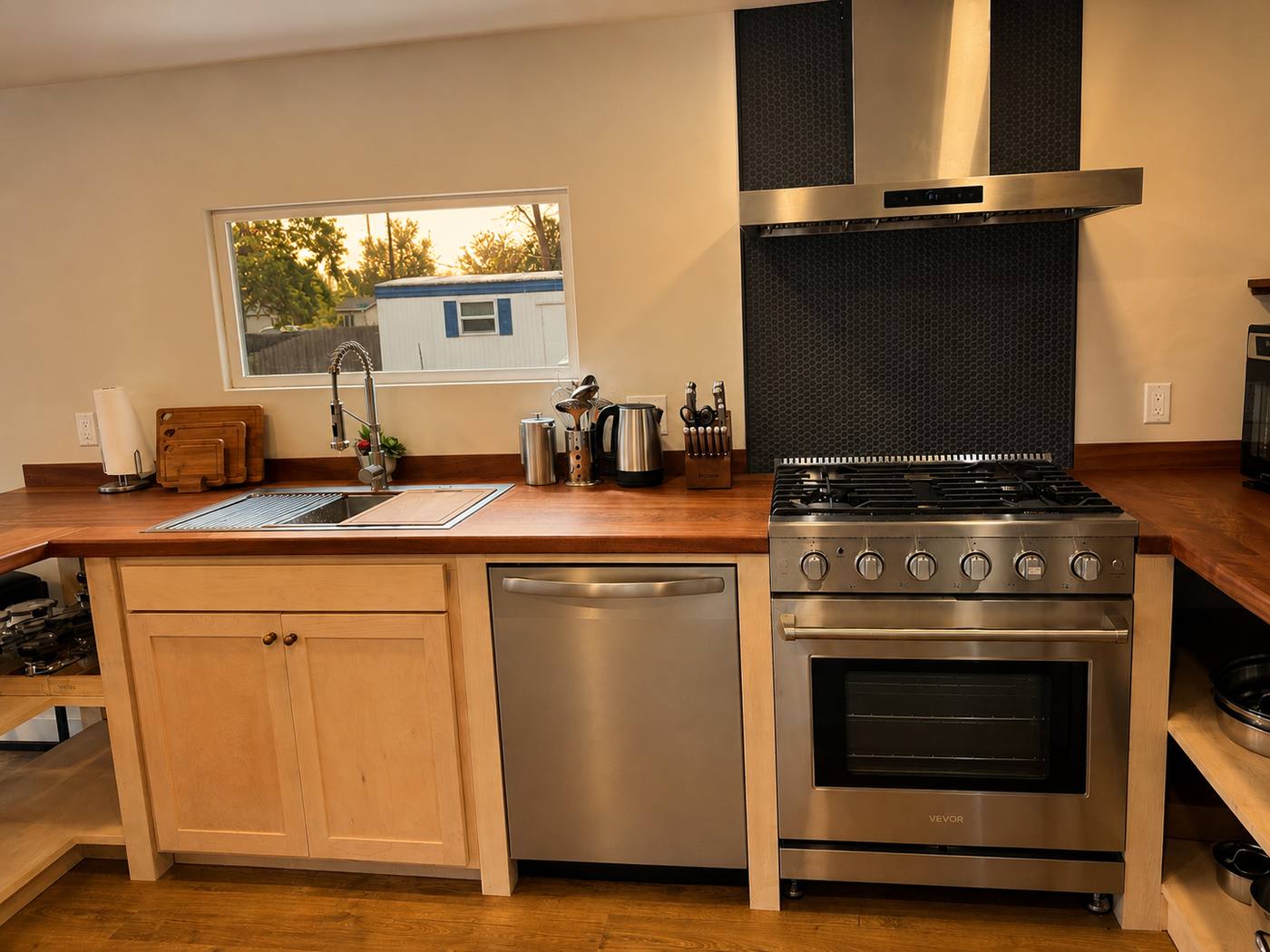 Stainless gas range and vent hood against a dark hexagonal tile backsplash