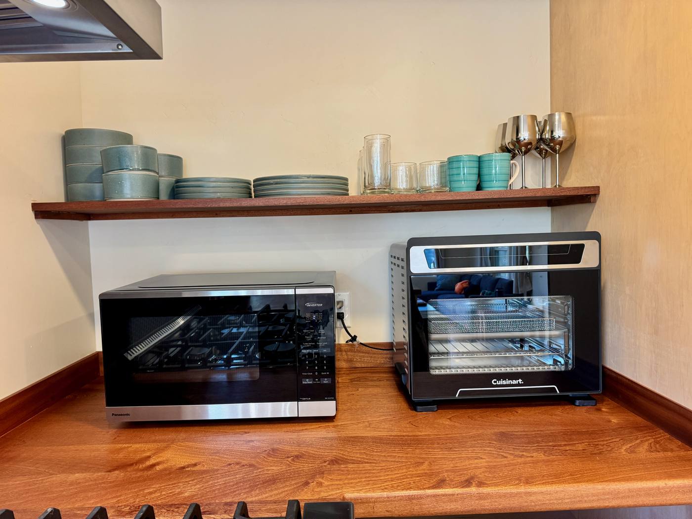 Microwave and countertop convection oven on the walnut counter, dishes and glassware on the shelf above