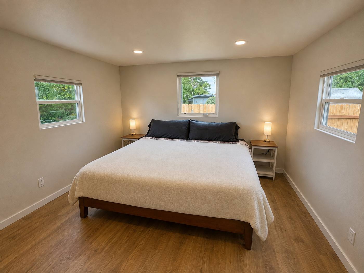 Bedroom in daylight with a king bed, matching nightstand lamps and windows on three walls