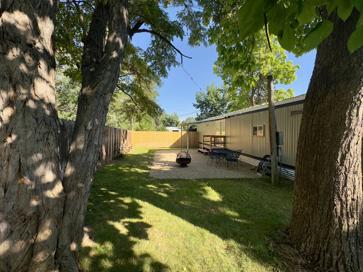 Back lawn shaded by two large trees, with a fire pit and seating on the gravel terrace