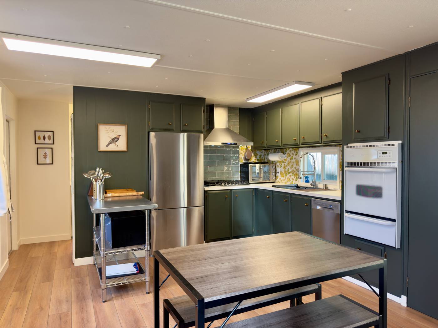 Kitchen with deep green cabinets, stainless refrigerator and a steel-topped prep island