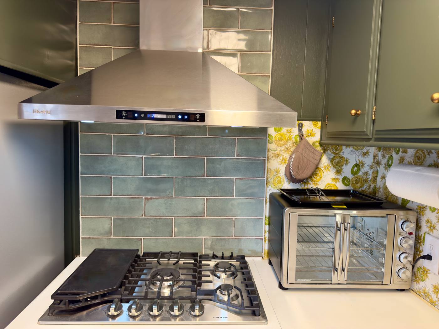 Gas cooktop with a stainless vent hood against a green tile backsplash