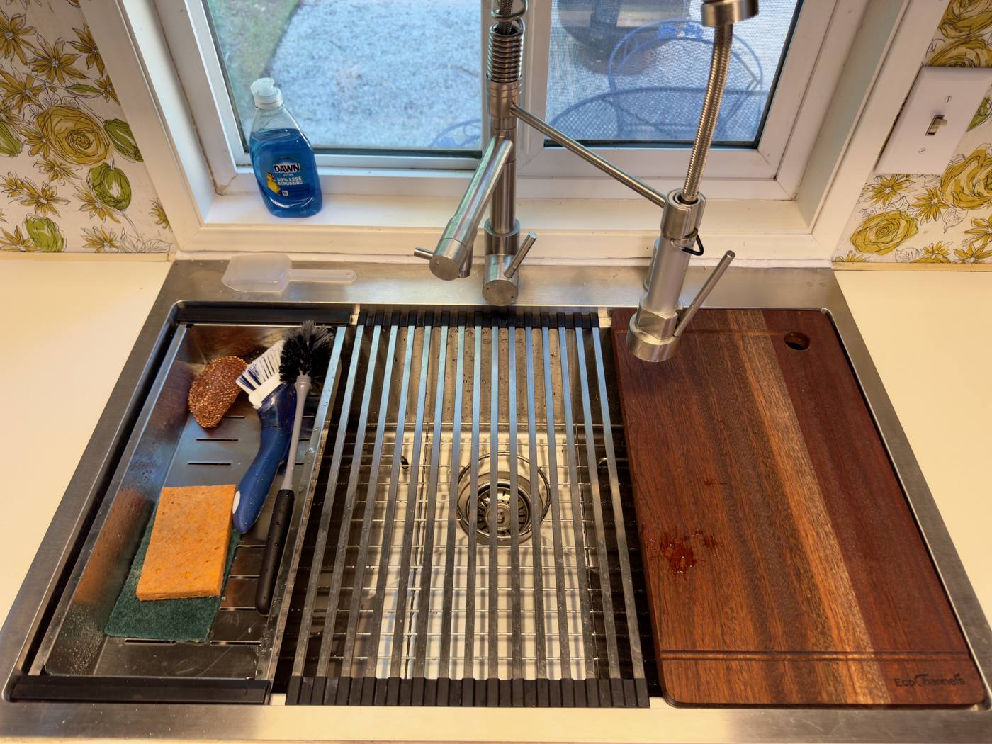 Deep kitchen sink with a hardwood cutting board and roll-up drying rack across it
