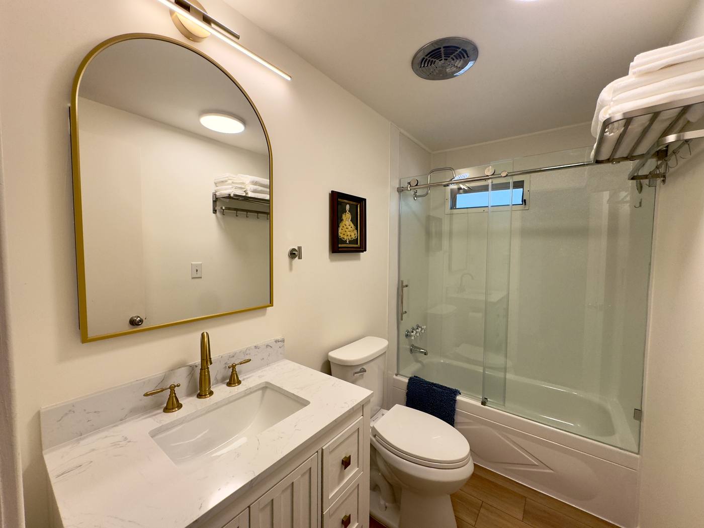 Second bathroom with an arched brass mirror, marble-topped vanity and glass-door tub and shower